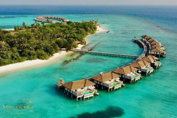 Aerial view of a tropical island in the Maldives with overwater villas extending into a turquoise lagoon.