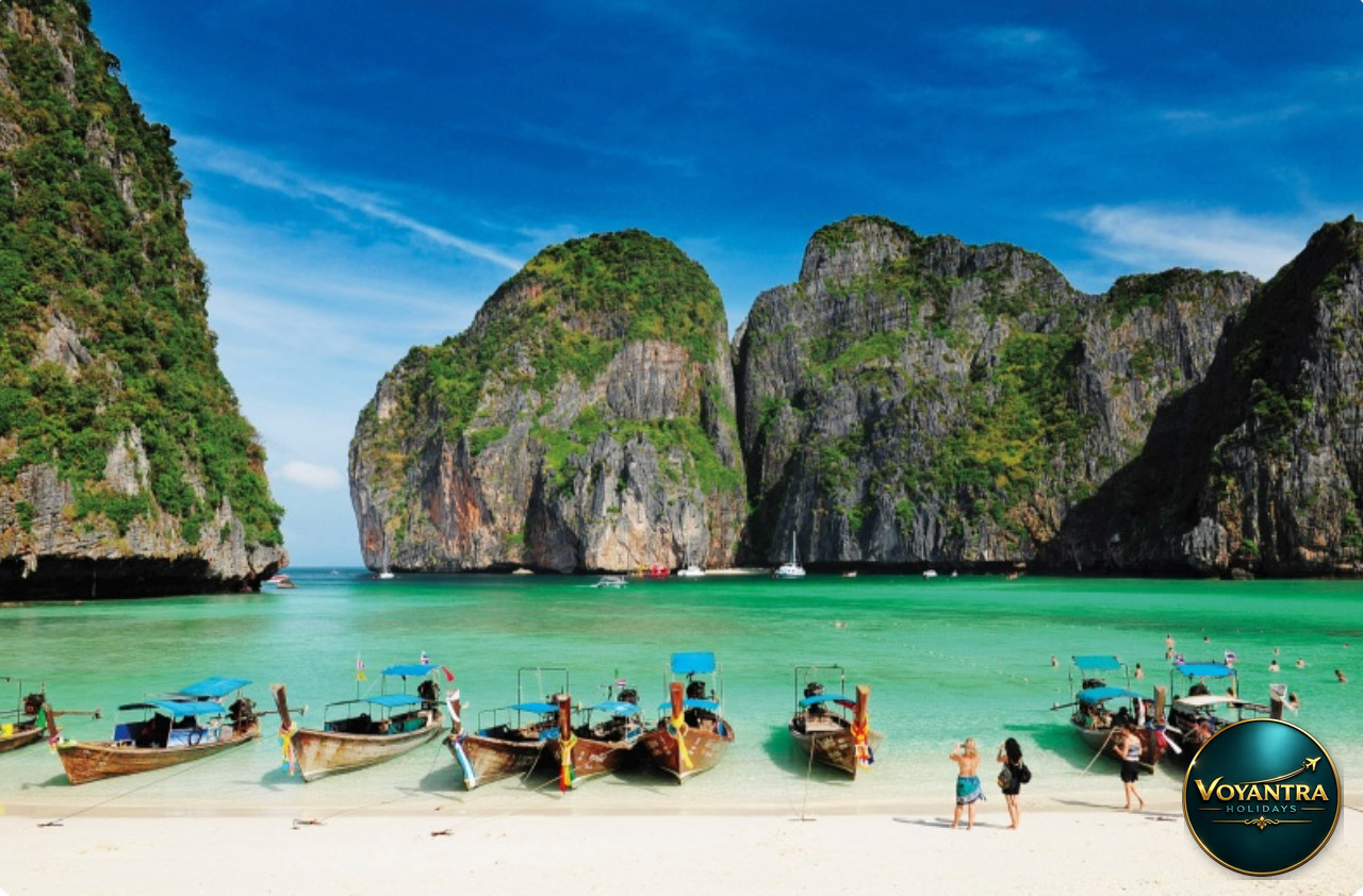 Traditional Thai long-tail boats on a tropical beach at Maya Bay, surrounded by limestone cliffs and turquoise water.